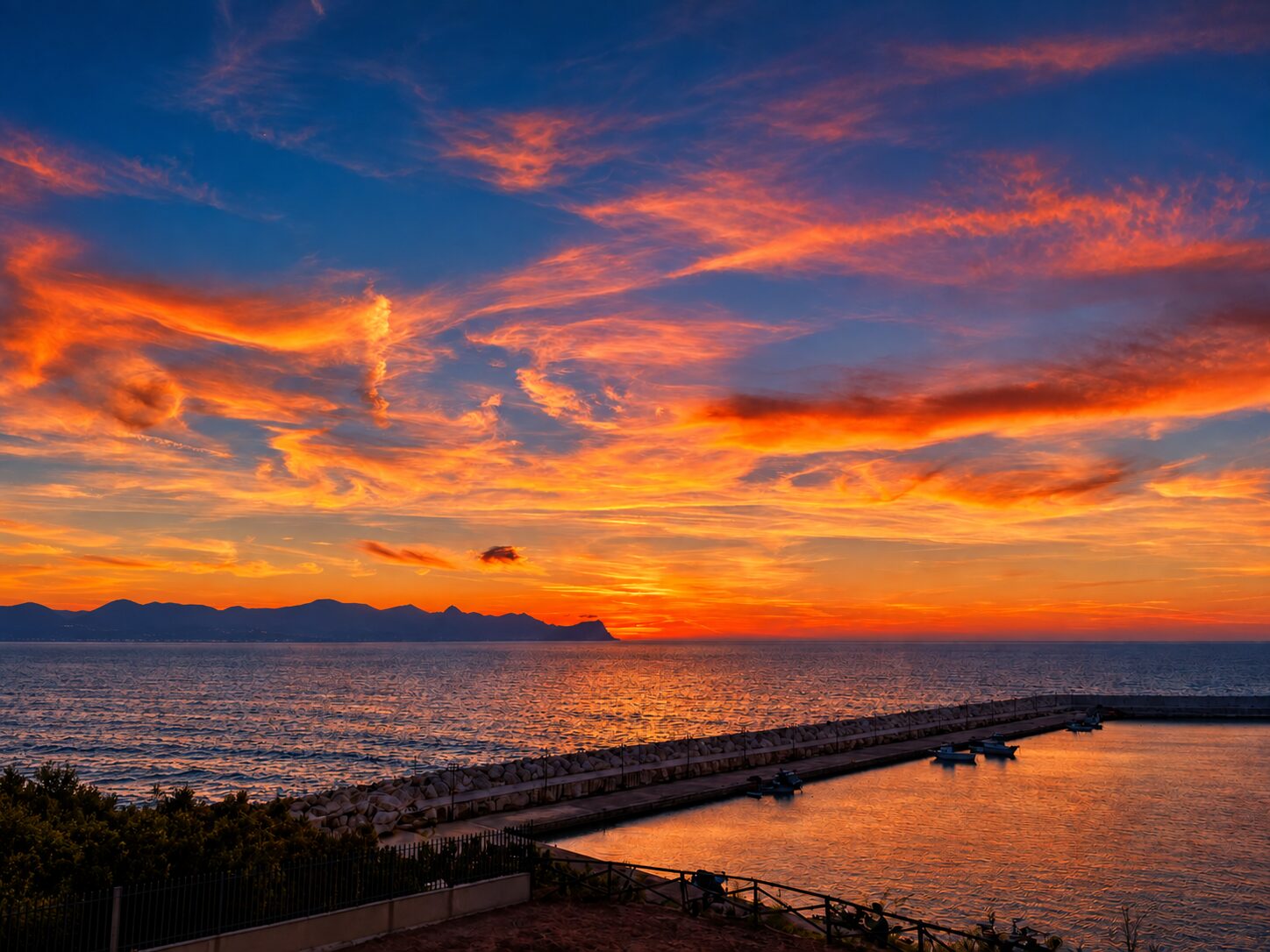 Orange sunset clouds above the sea and harbour of Balestrate